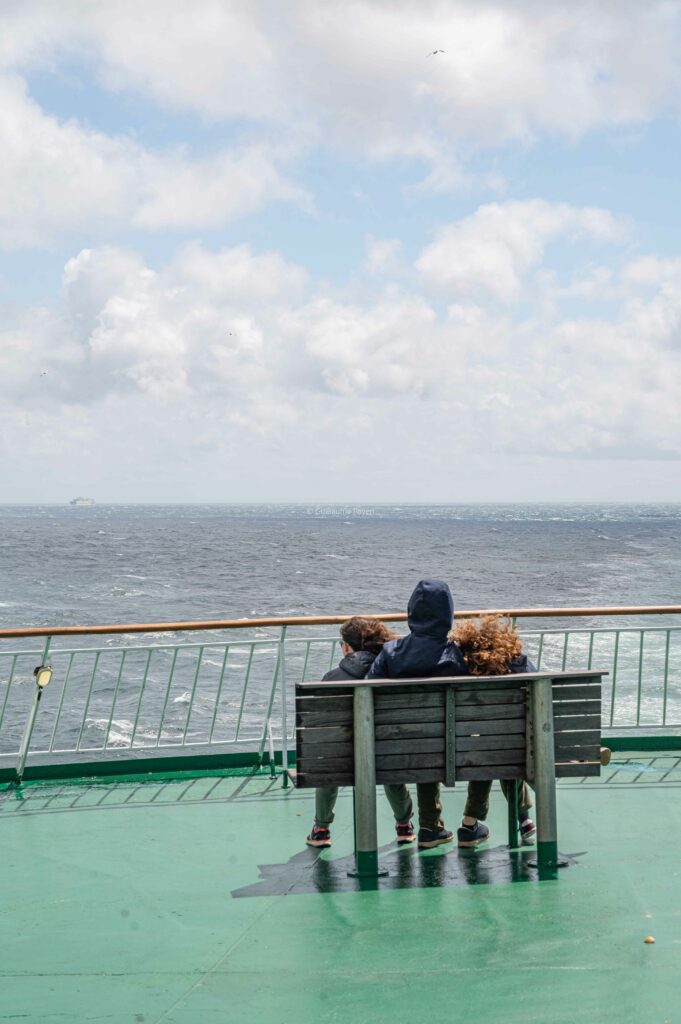 on voit une famille sur un banc sur le toit du ferry observant la mer 