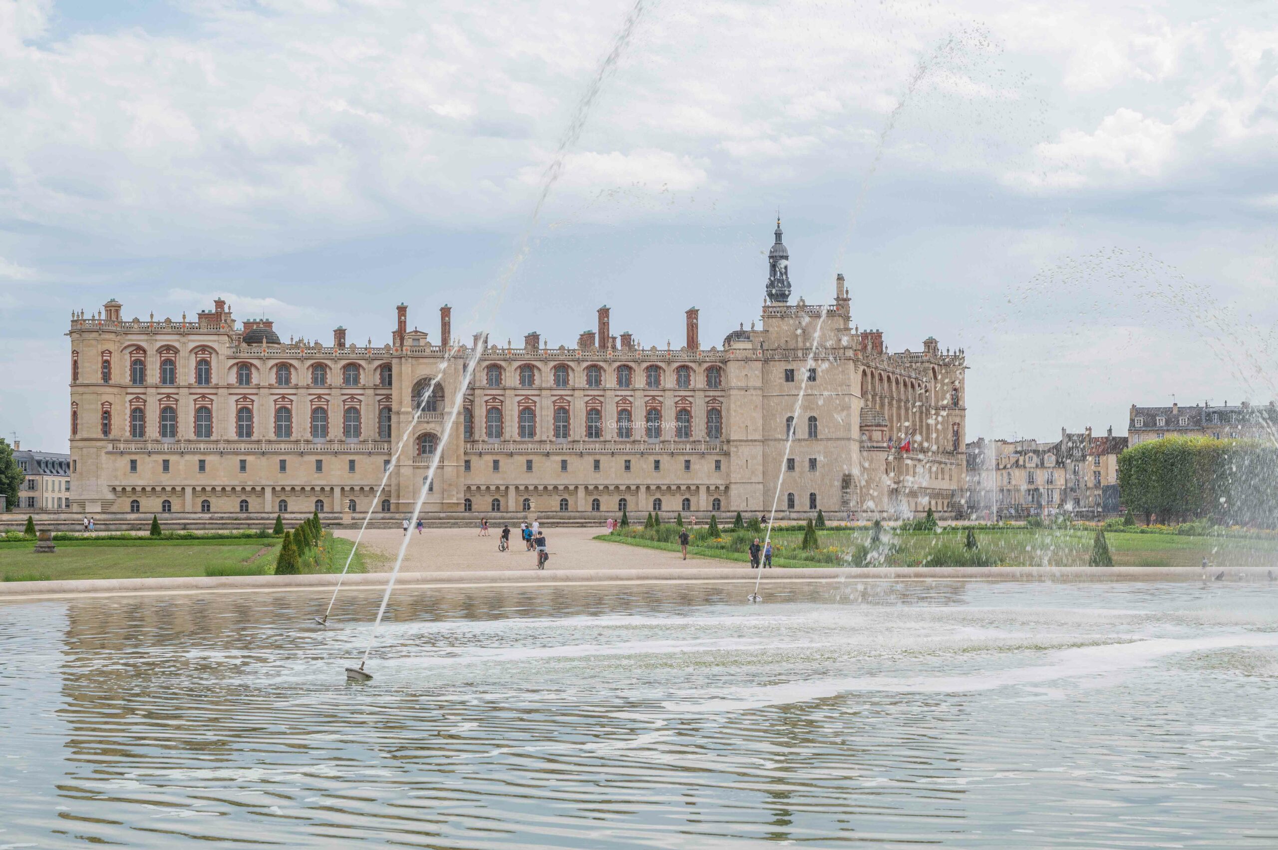 Le château avec devant une fontaine et un bassin avec au loin des vélos 